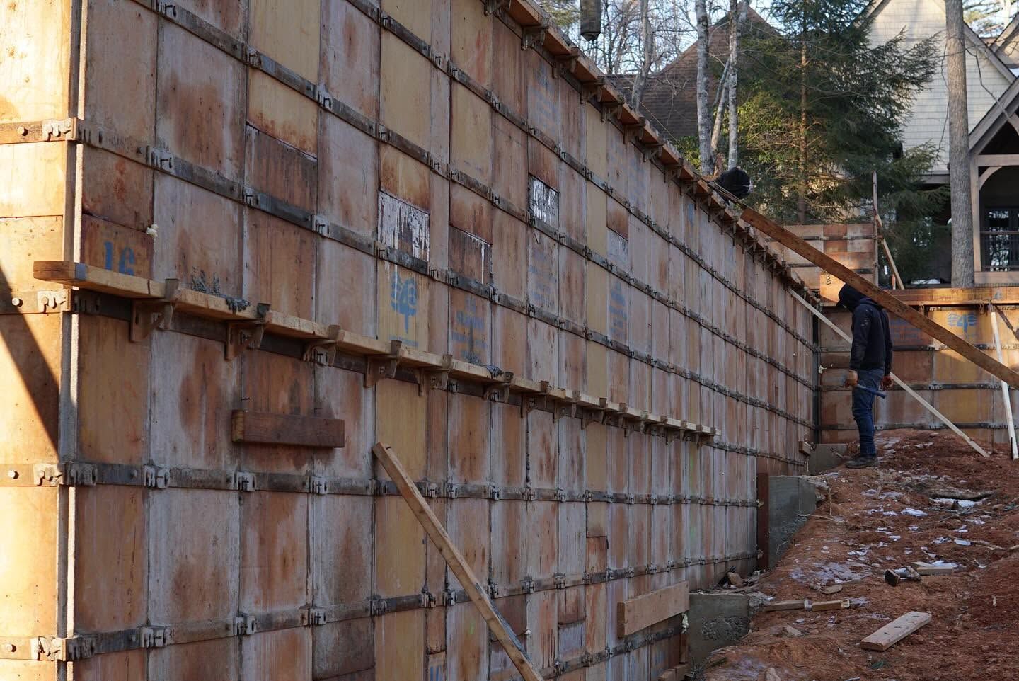 Large rusted retaining wall with wooden braces on a construction site, a person standing at right.