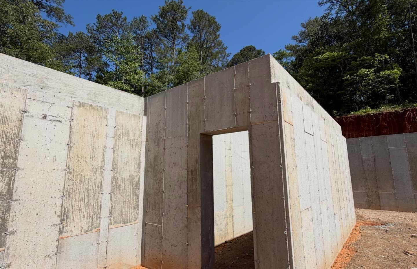 Concrete foundation walls at a construction site with a doorway opening and trees in the background