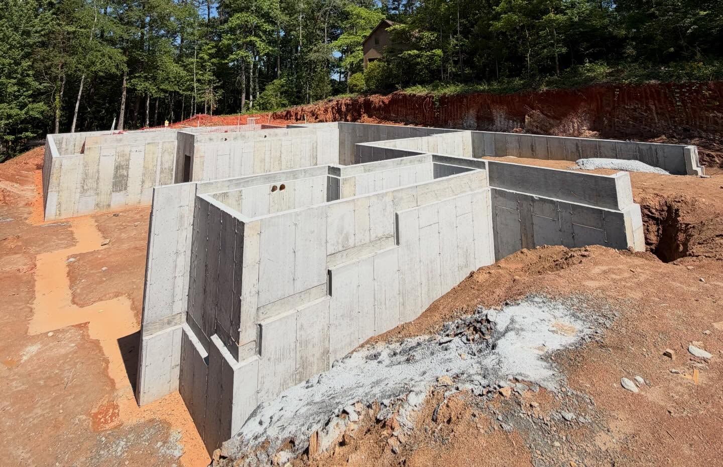 Concrete foundation walls under construction on a dirt site with trees in the background
