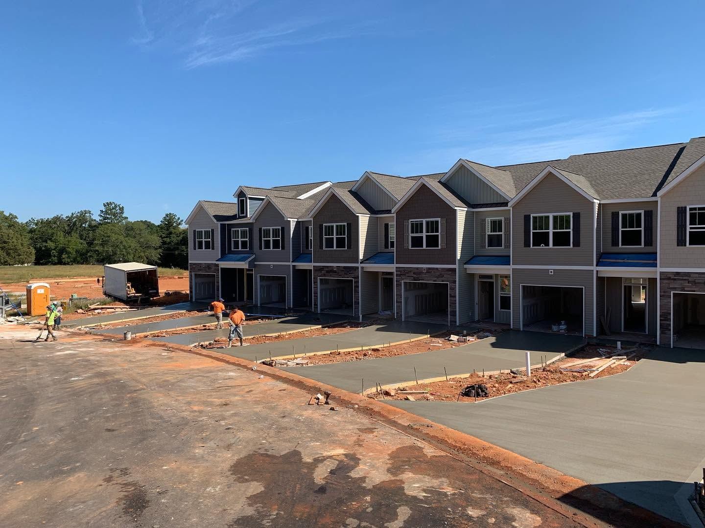 Row of townhouses under construction with workers, concrete driveways, and scattered bricks on a sunny day