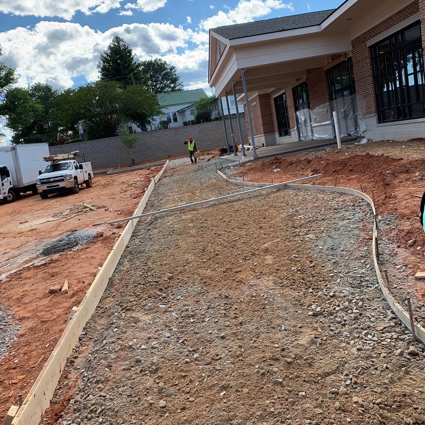 Gravel walkway under construction beside a house, with workers, a truck, and red dirt around it