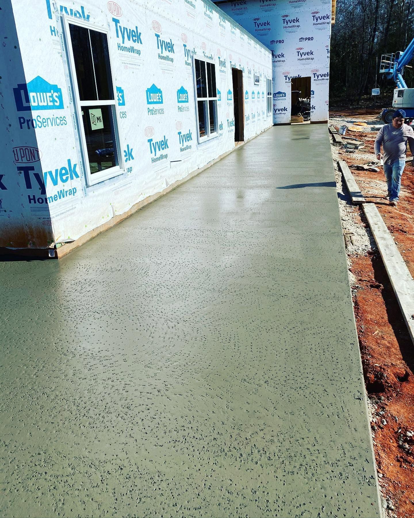 Concrete walkway beside a white Tyvek-wrapped building under construction