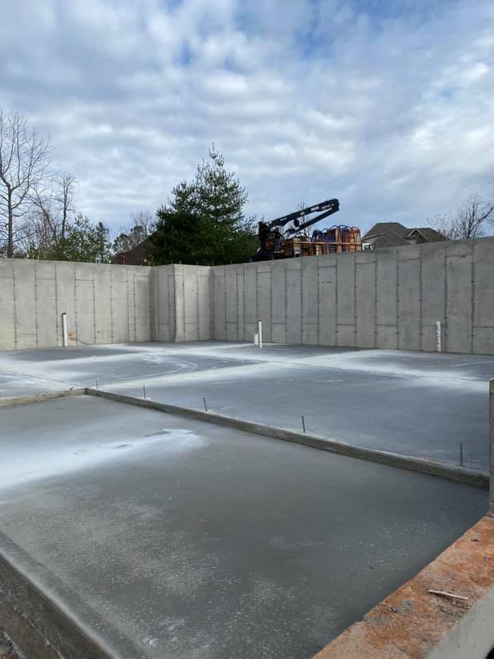 Concrete foundation slab surrounded by tall gray retaining walls under a cloudy sky