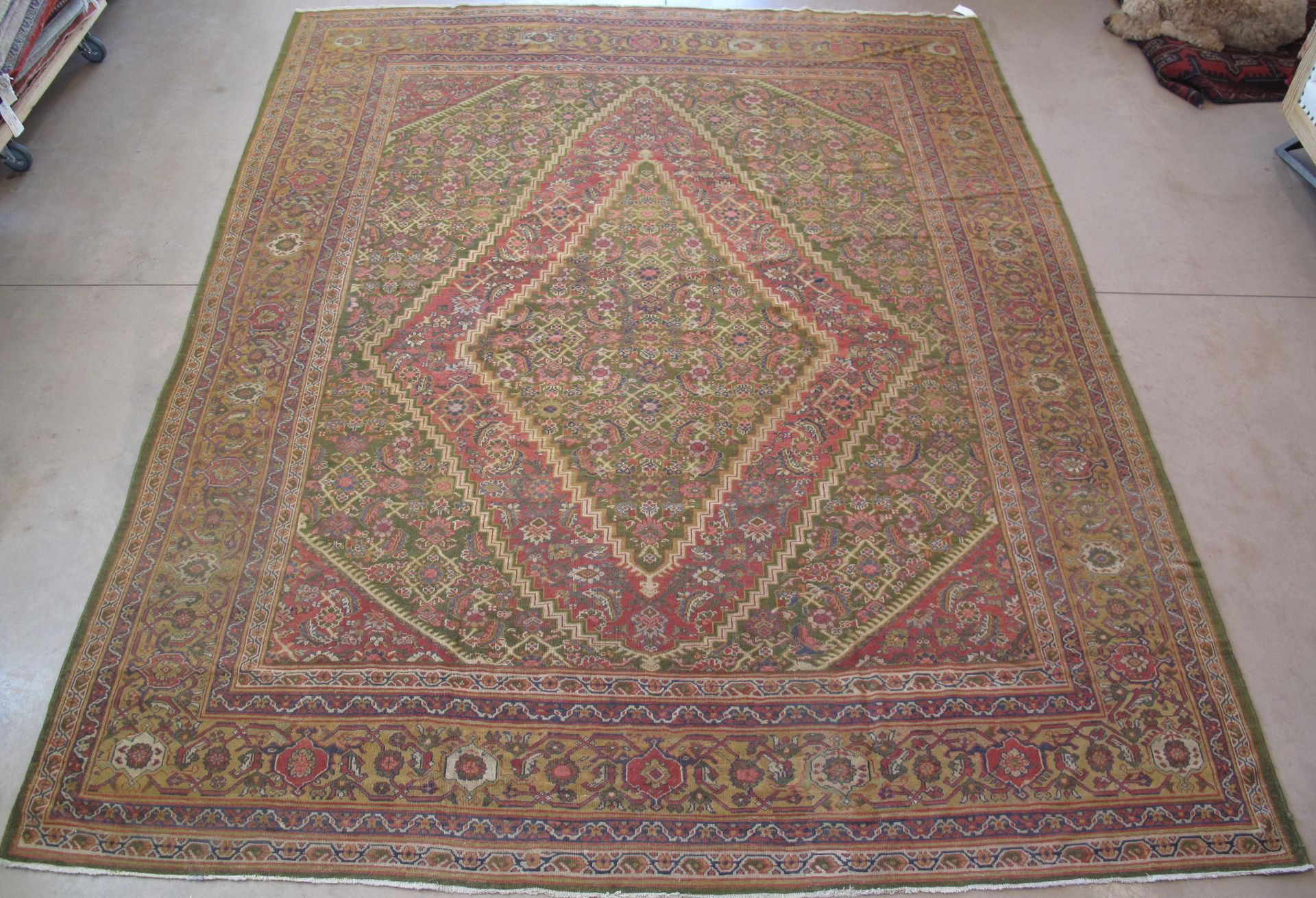 Large, ornate Persian rug with a central diamond design in red and beige, on a green field.