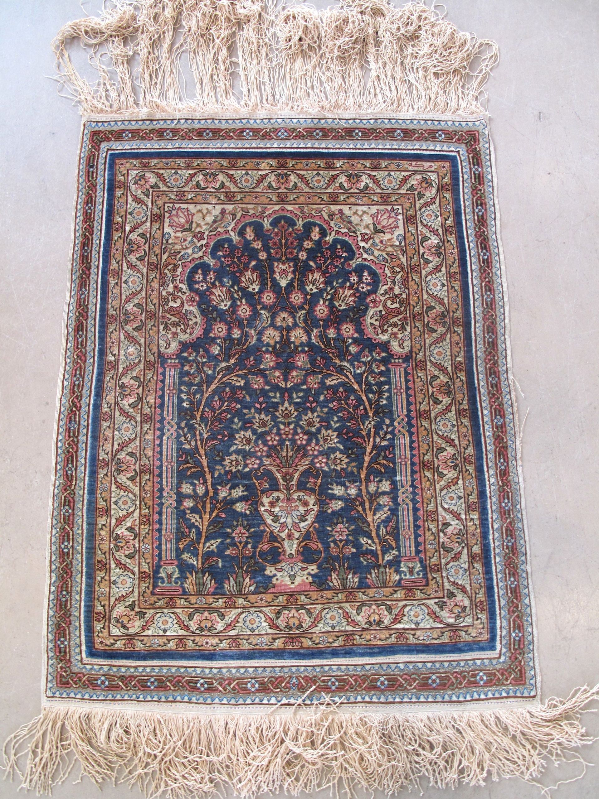 A rug with a floral pattern and fringe is hanging on a wall
