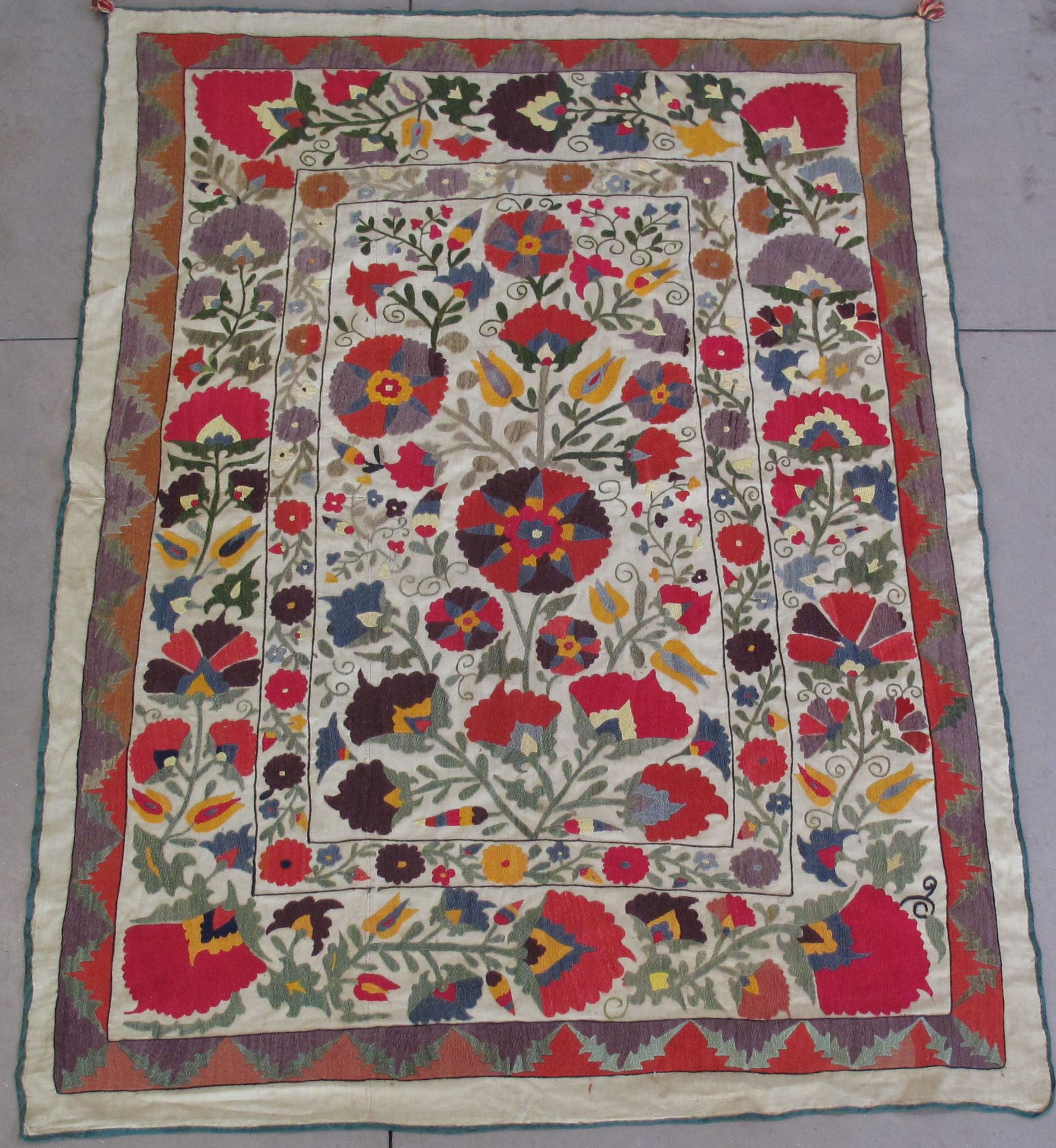 Colorful embroidered textile with floral designs and geometric border.