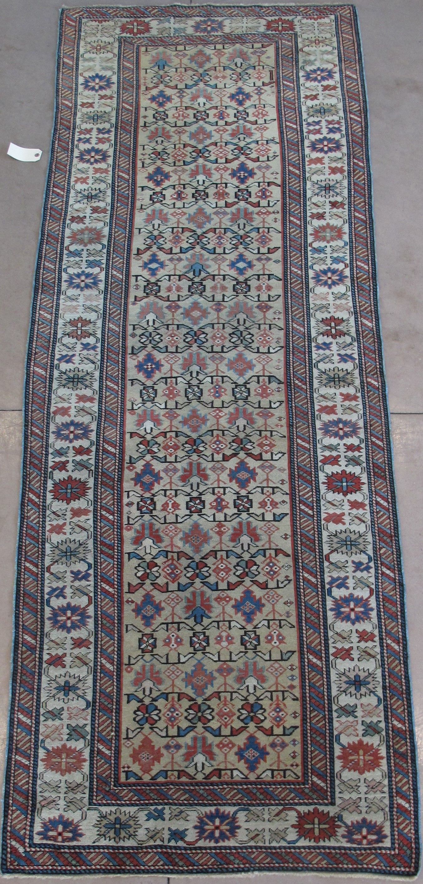 Long, rectangular rug with a cream field, red, blue, and brown geometric patterns, and a border.