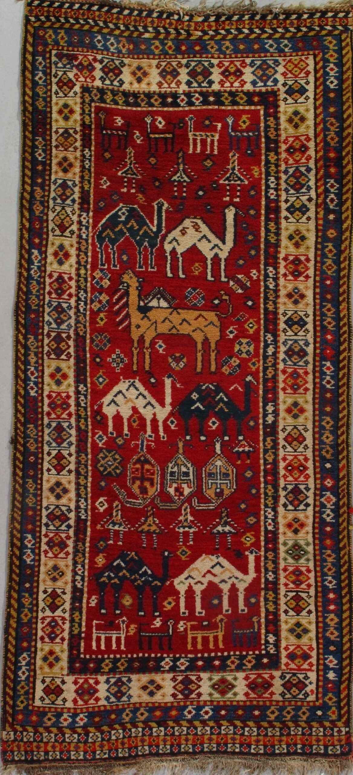 A red rug with camels on it is hanging on a wall.