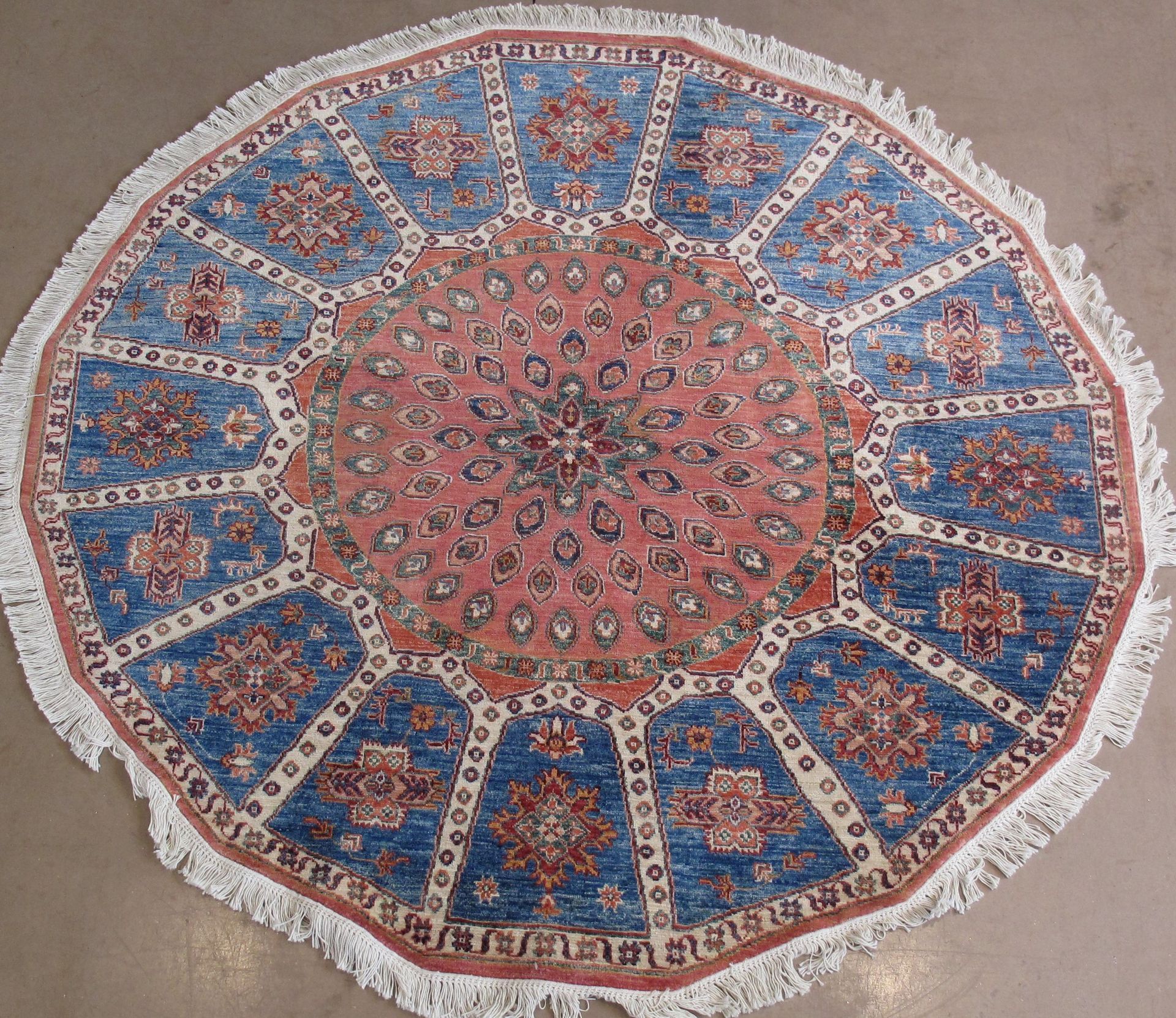 Round rug with a blue and red geometric pattern and fringe.