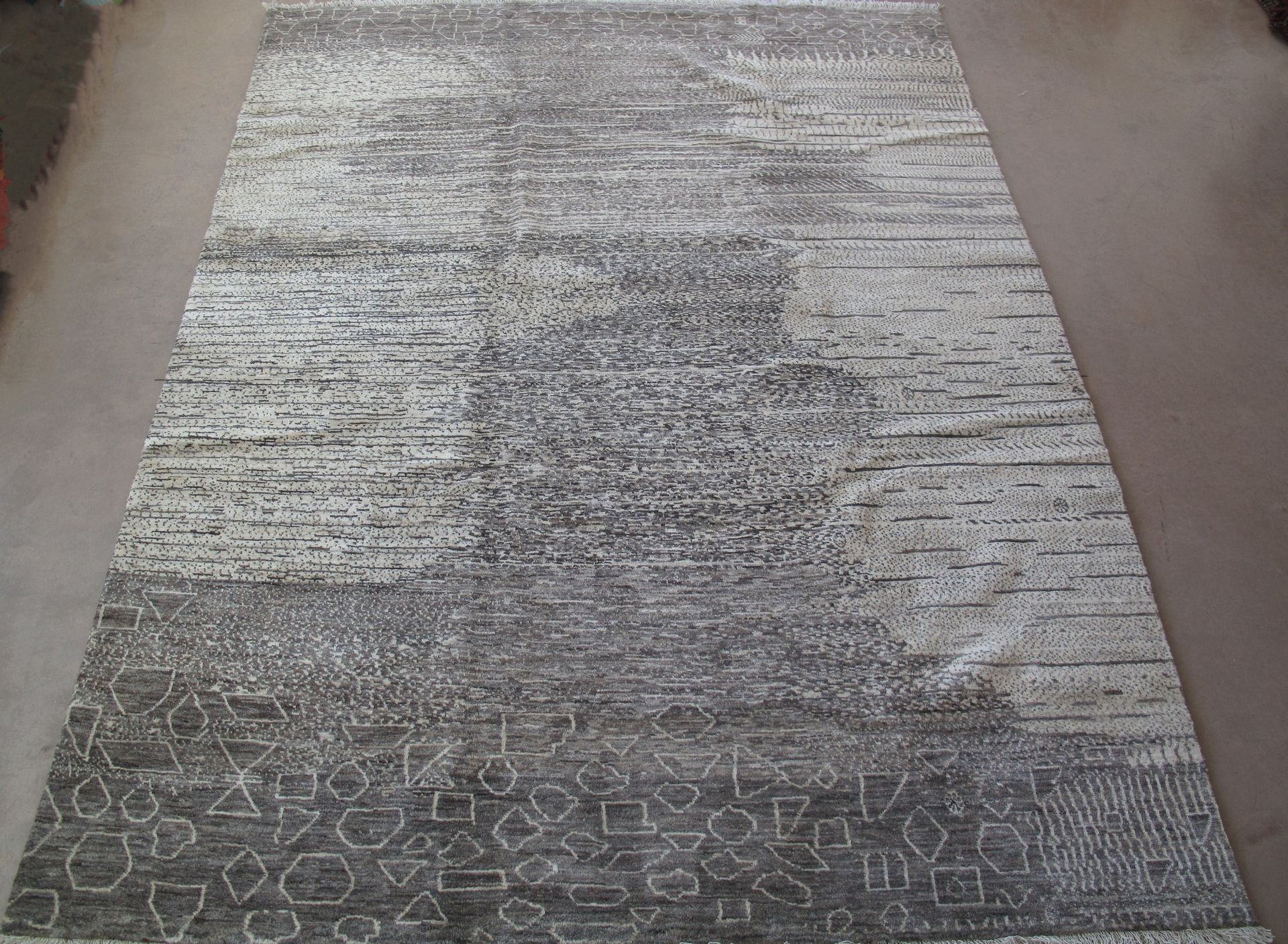 A gray and white rug is sitting on a carpeted floor.