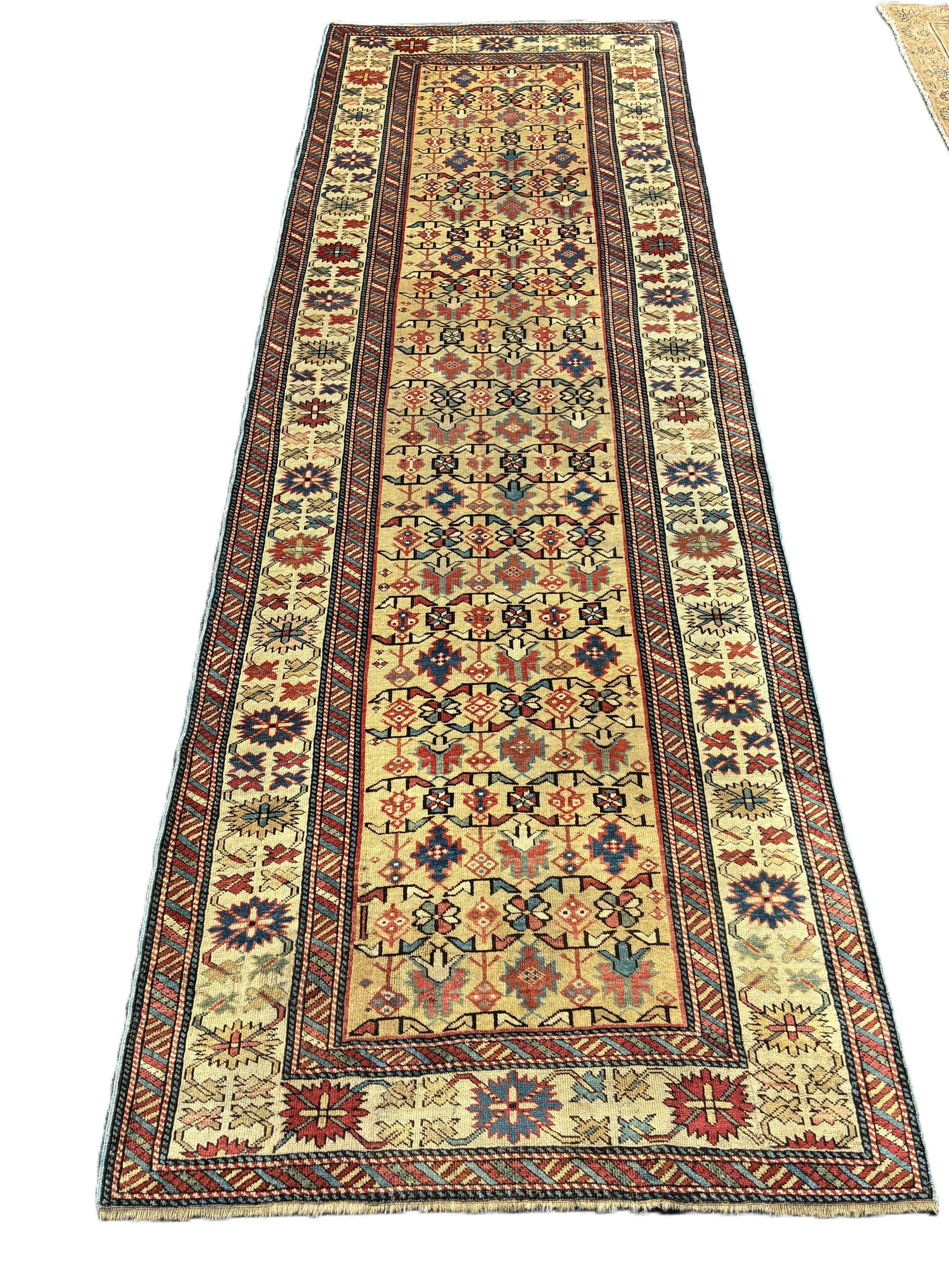Long, rectangular rug with a cream field, red, blue, and brown geometric patterns, and a border.