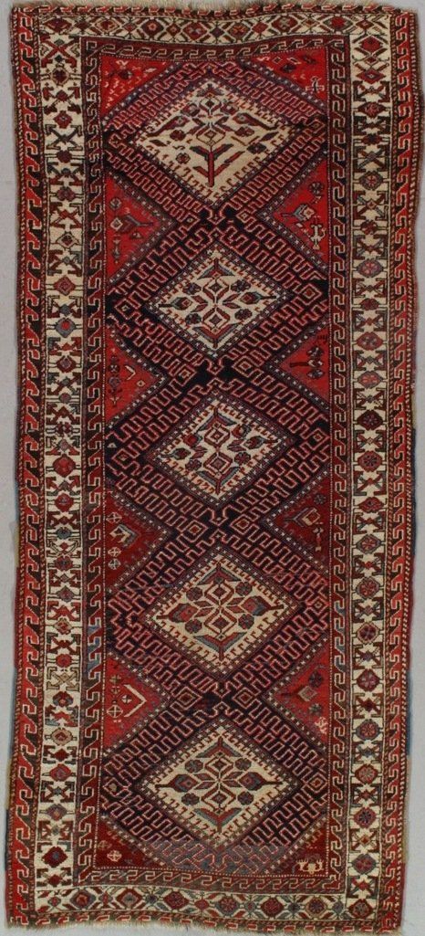 A red rug with a pattern on it is sitting on a white surface.