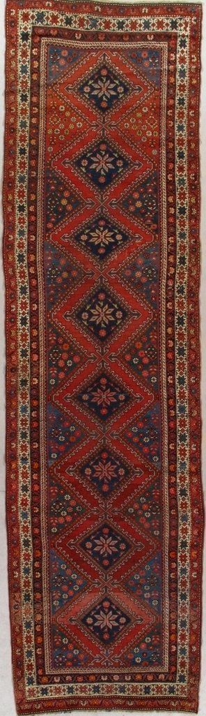 A red rug with a geometric pattern is hanging on a wall.