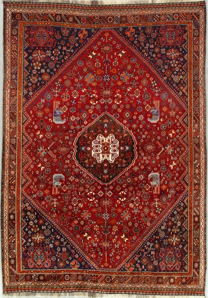 A red rug with a floral pattern on it is hanging on a wall.