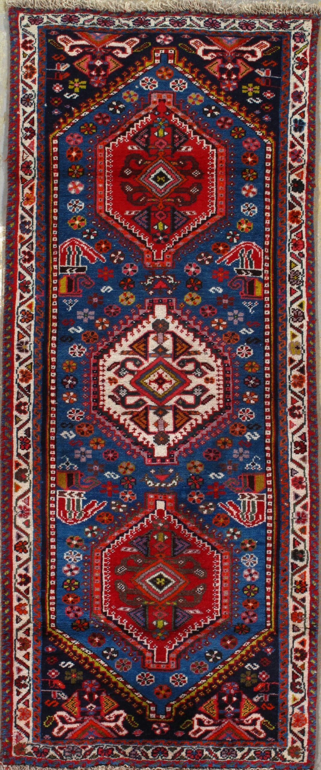A blue and red rug with a pattern on it is hanging on a wall.