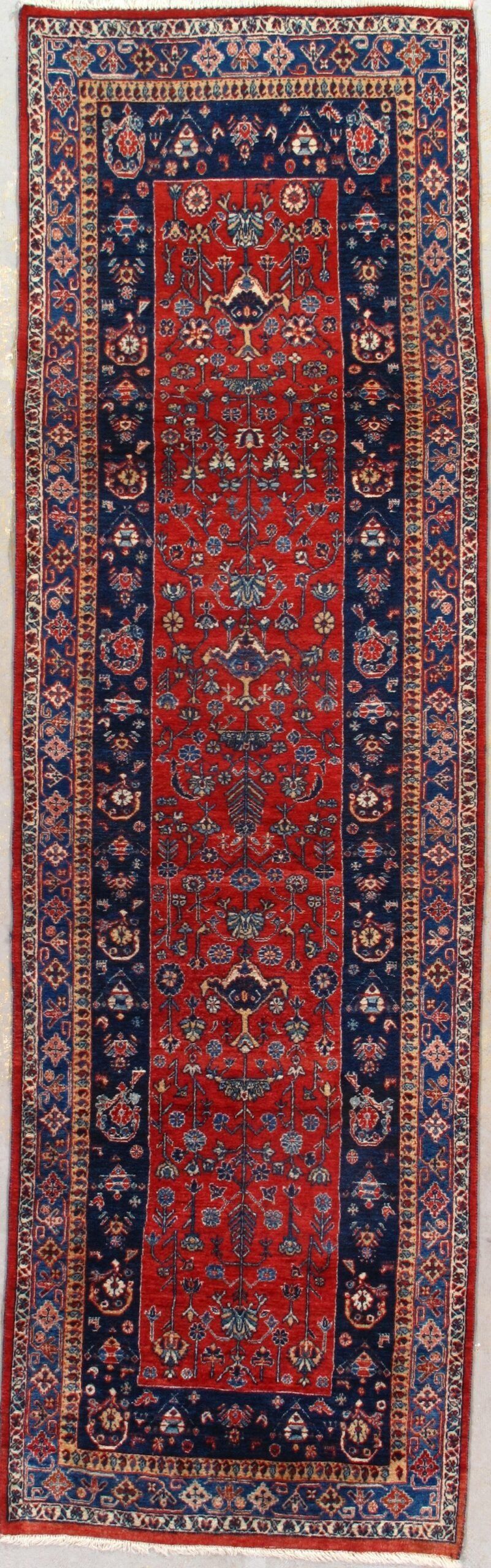 A red and blue rug is hanging on a white wall.