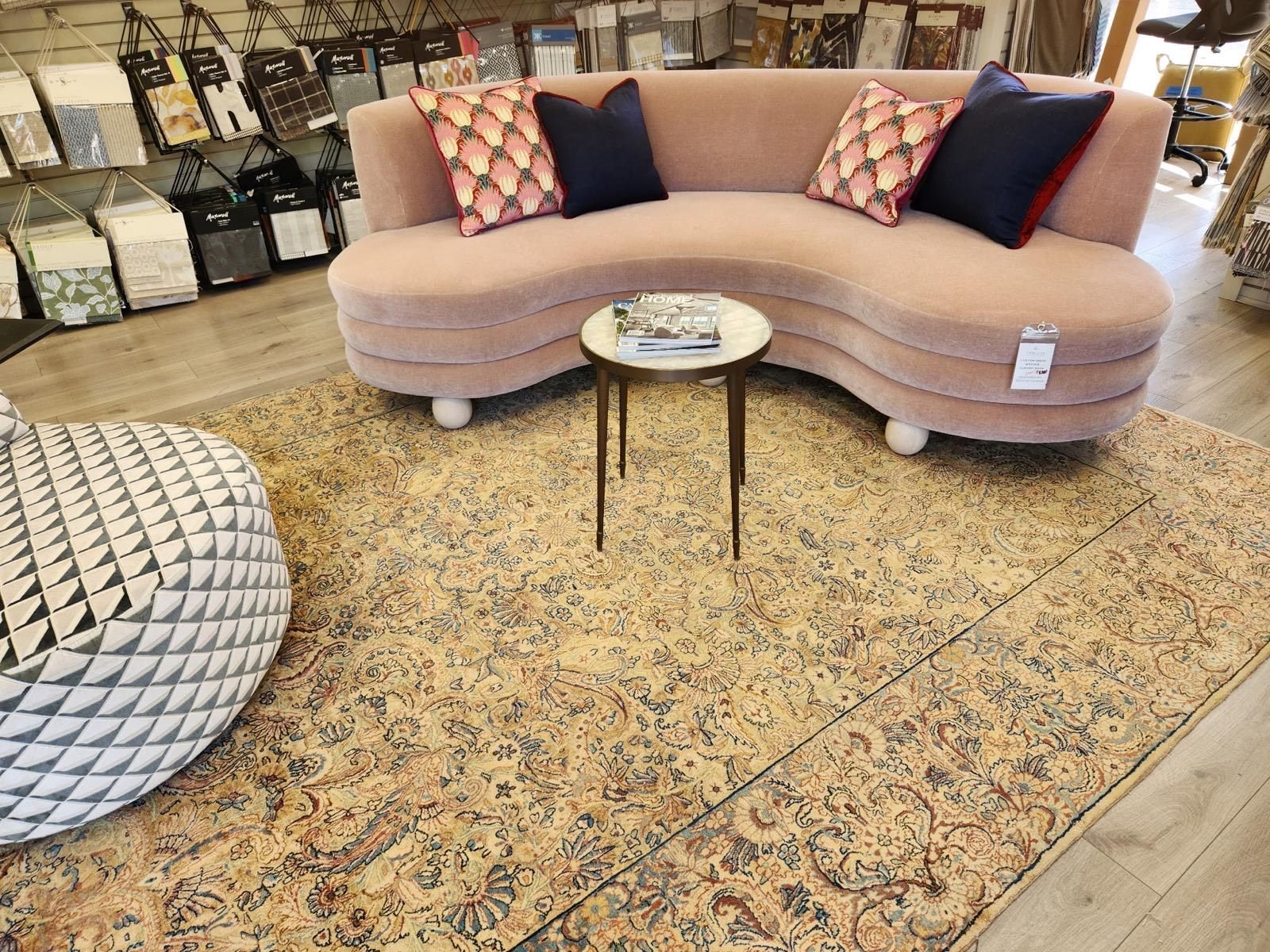 Pink curved sofa with patterned pillows on a vintage rug in a showroom.