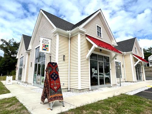 A large house with a red awning and a rug on the sidewalk in front of it.