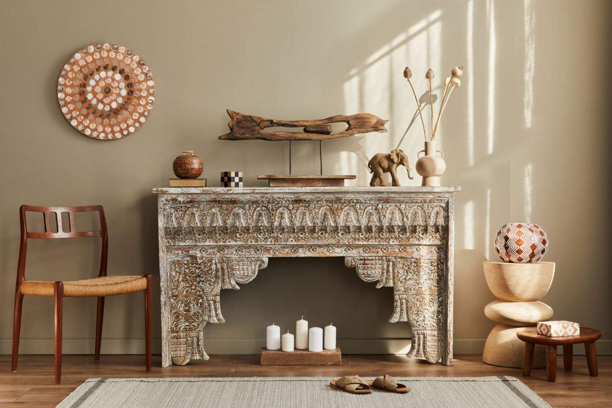 Carved white mantel with decor, chair, heirloom rug, and objects on beige wall.