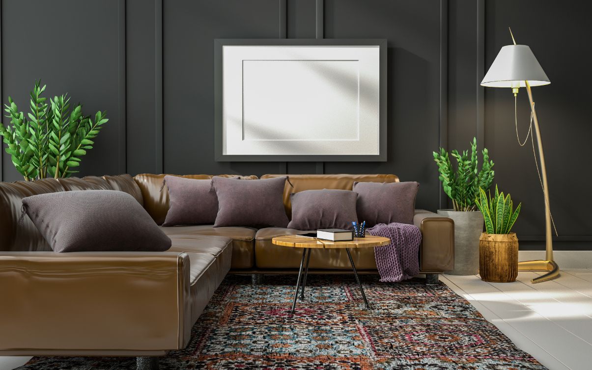 Leather sectional sofa in a room with a dark wall, persian rug, plants, and a framed picture.