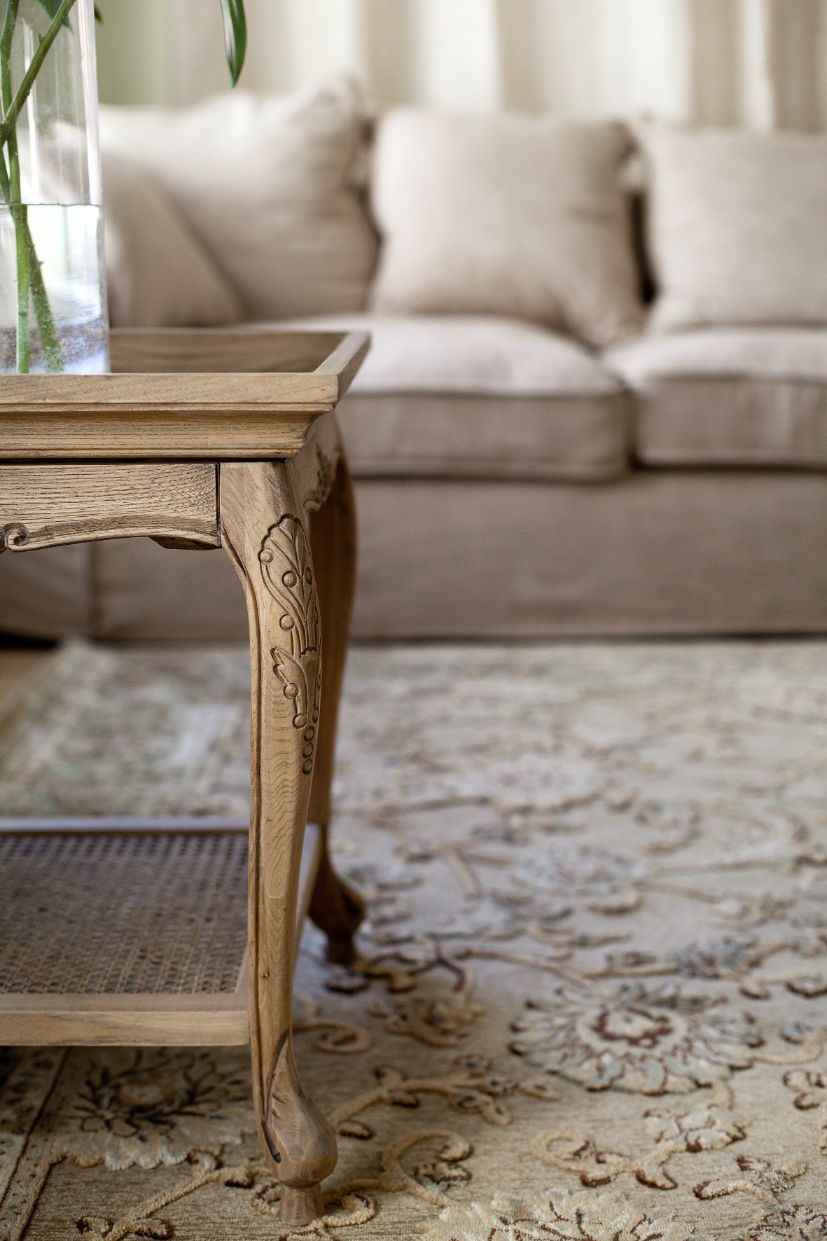 Wooden side table with floral detail; neutral sofa and patterned rug in background.