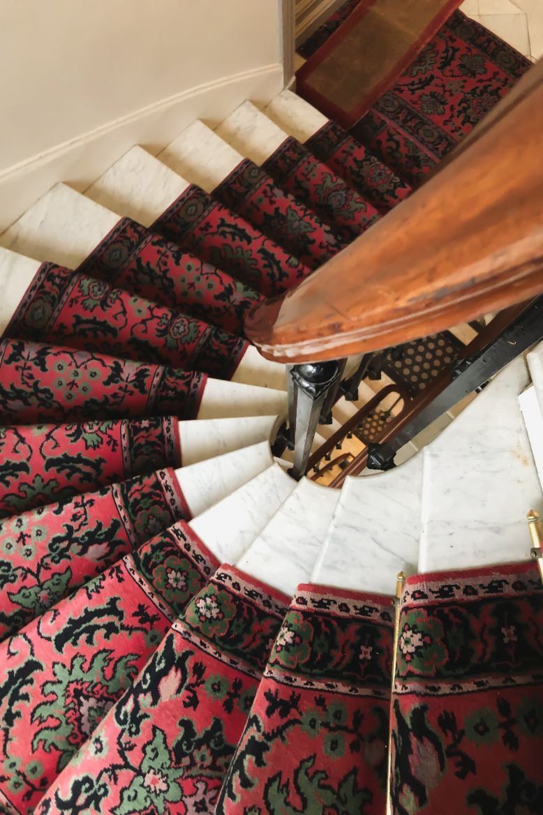 Spiral staircase with red patterned carpet runner on white steps, wooden handrail.