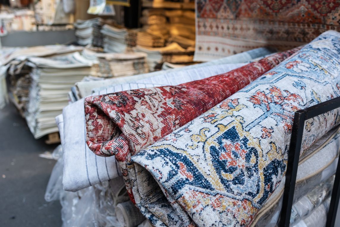 Rolled rugs with intricate patterns in red, blue, and white; market display.