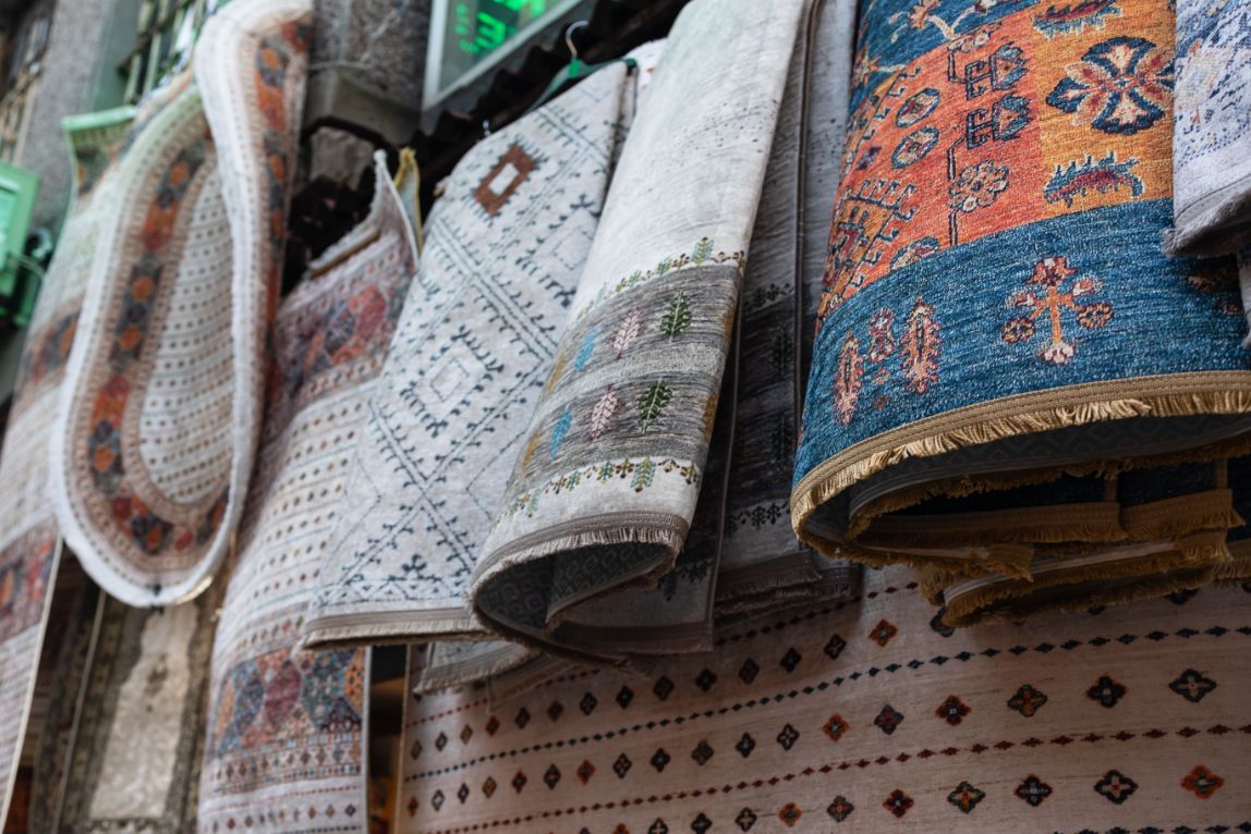 Rolled-up, patterned rugs hanging for display; various colors, including blues, oranges, and whites.