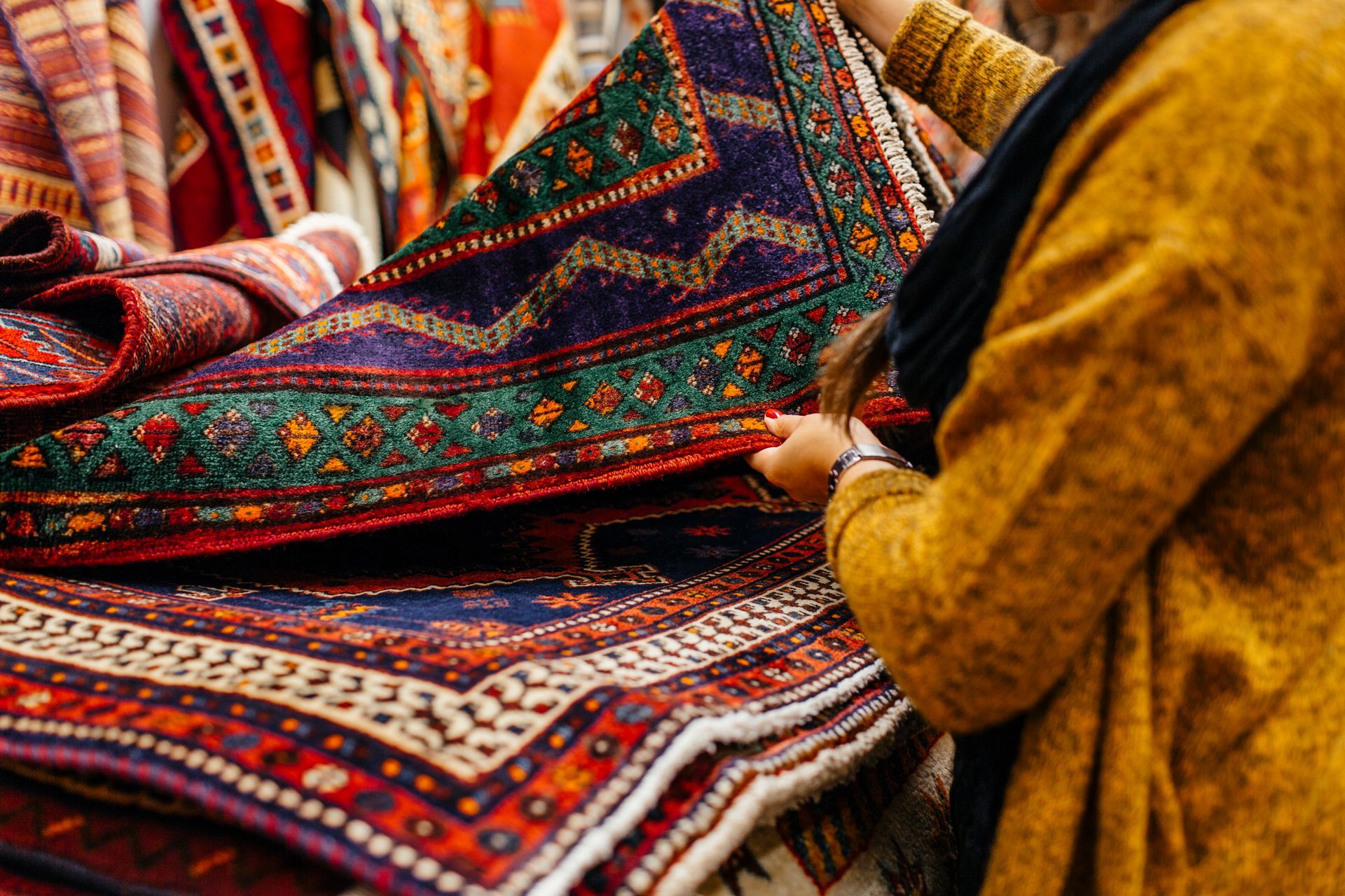 A woman is holding a colorful rug in her hands.