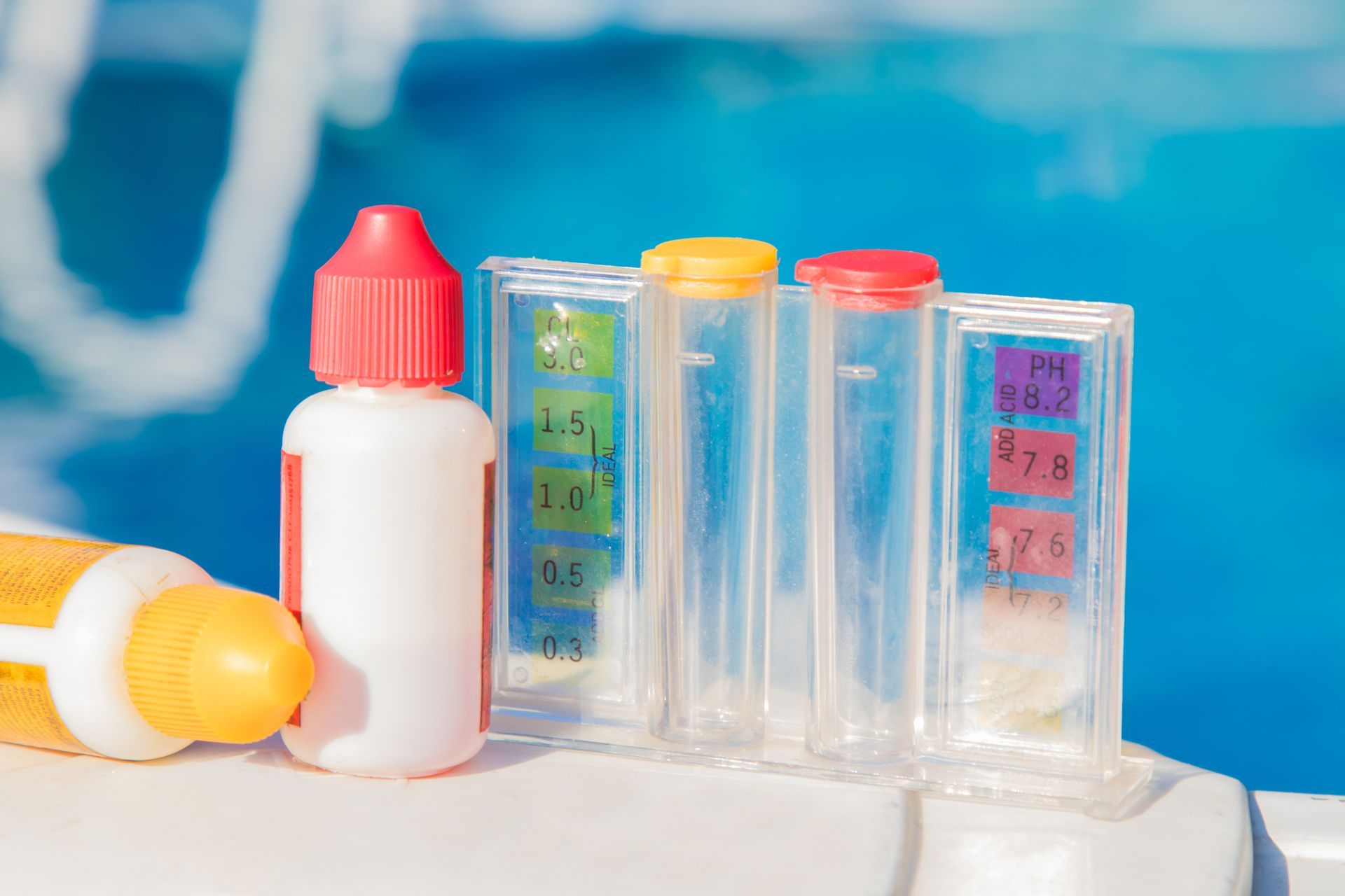 Pool testing kit with reagent drops and test tubes, blue pool water in background.