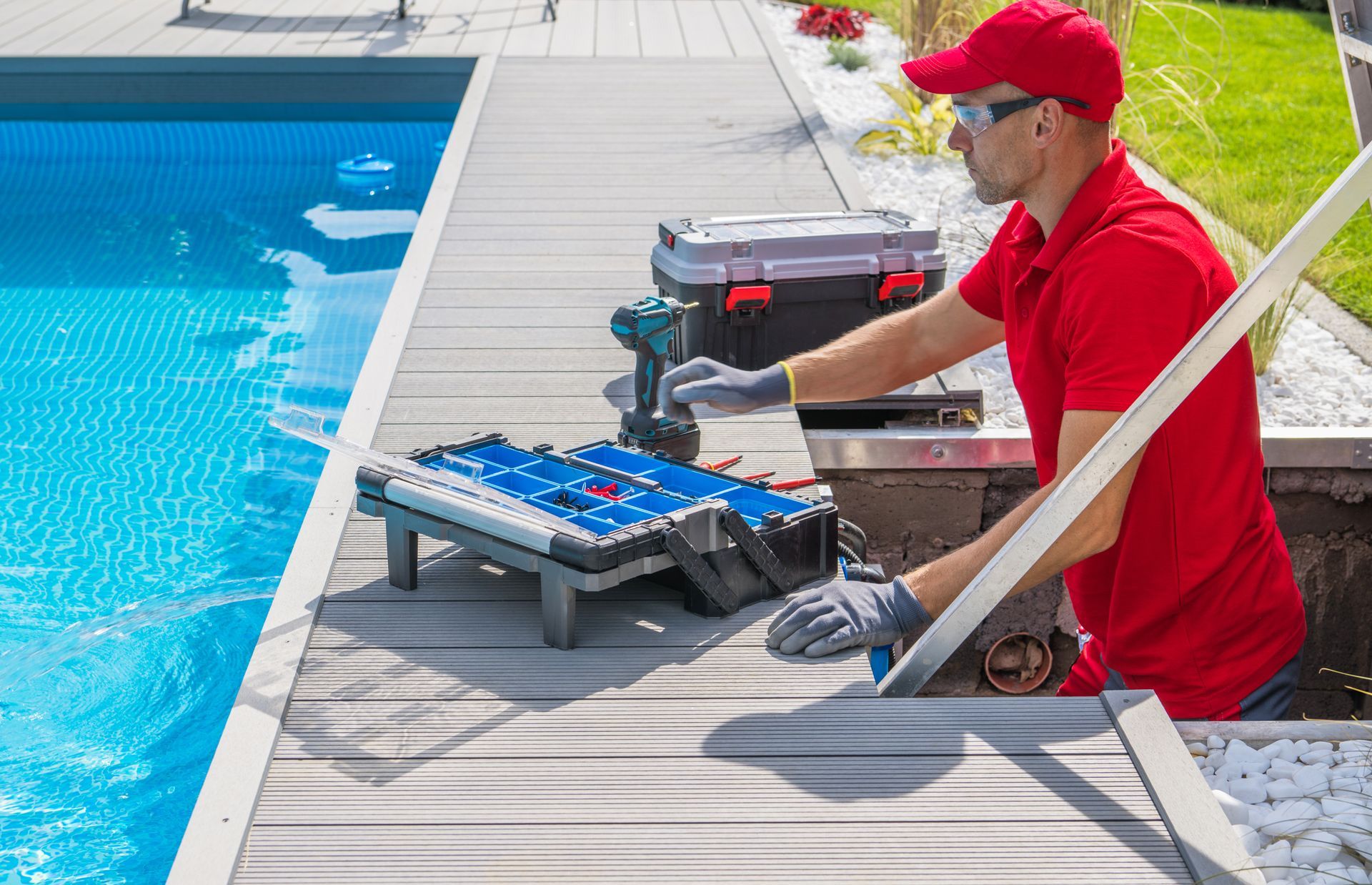Man in red shirt and cap repairing pool equipment by pool.