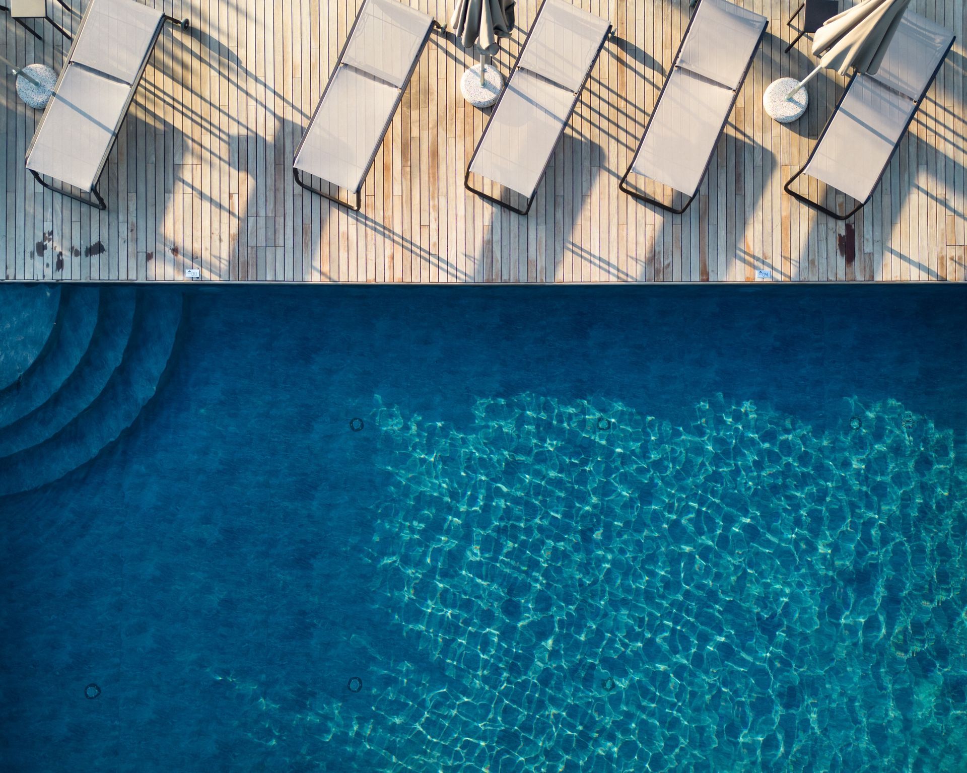 Poolside view of a pool with steps, wooden deck, and lounge chairs.