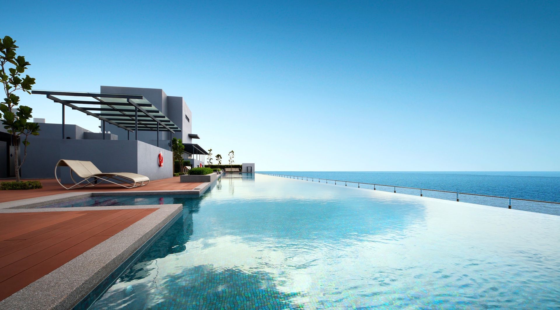 Infinity pool overlooking ocean, with lounge chair and modern building.
