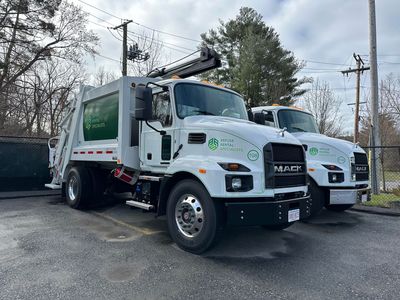 Two garbage trucks are parked next to each other in a parking lot.