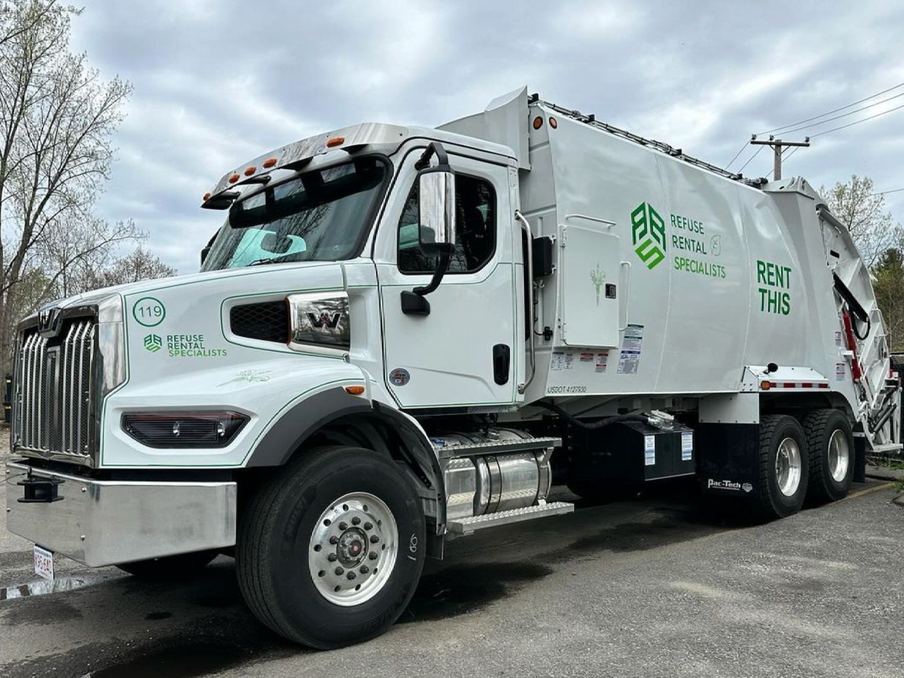 A white garbage truck is parked in front of a green building.