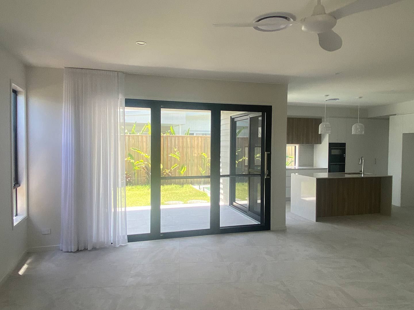 An Empty Living Room With Sliding Glass Doors and a Ceiling Fan — Curtain Concepts in Banora Point, NSW