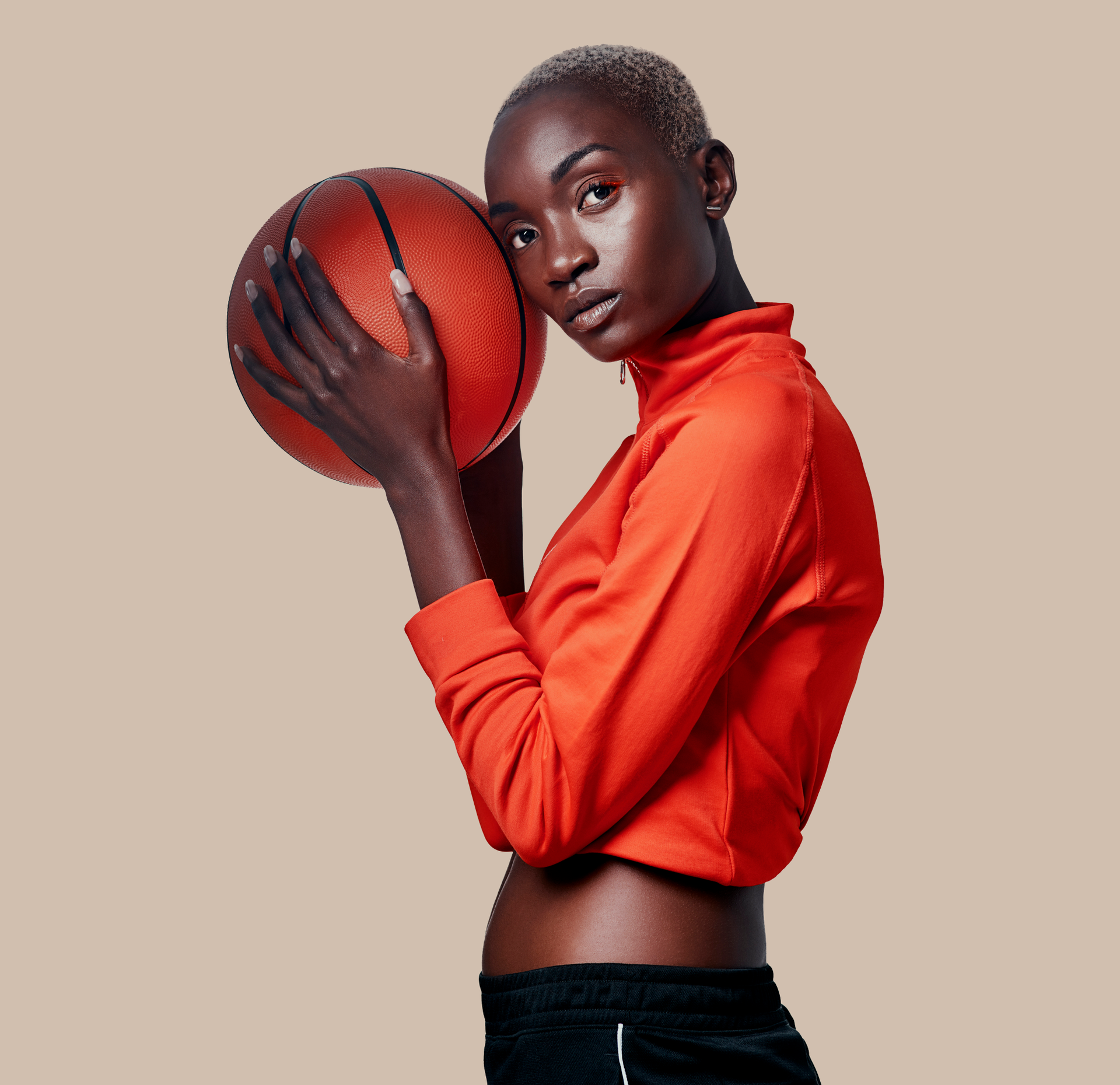 Person holding a basketball, wearing an orange top against a plain beige background.