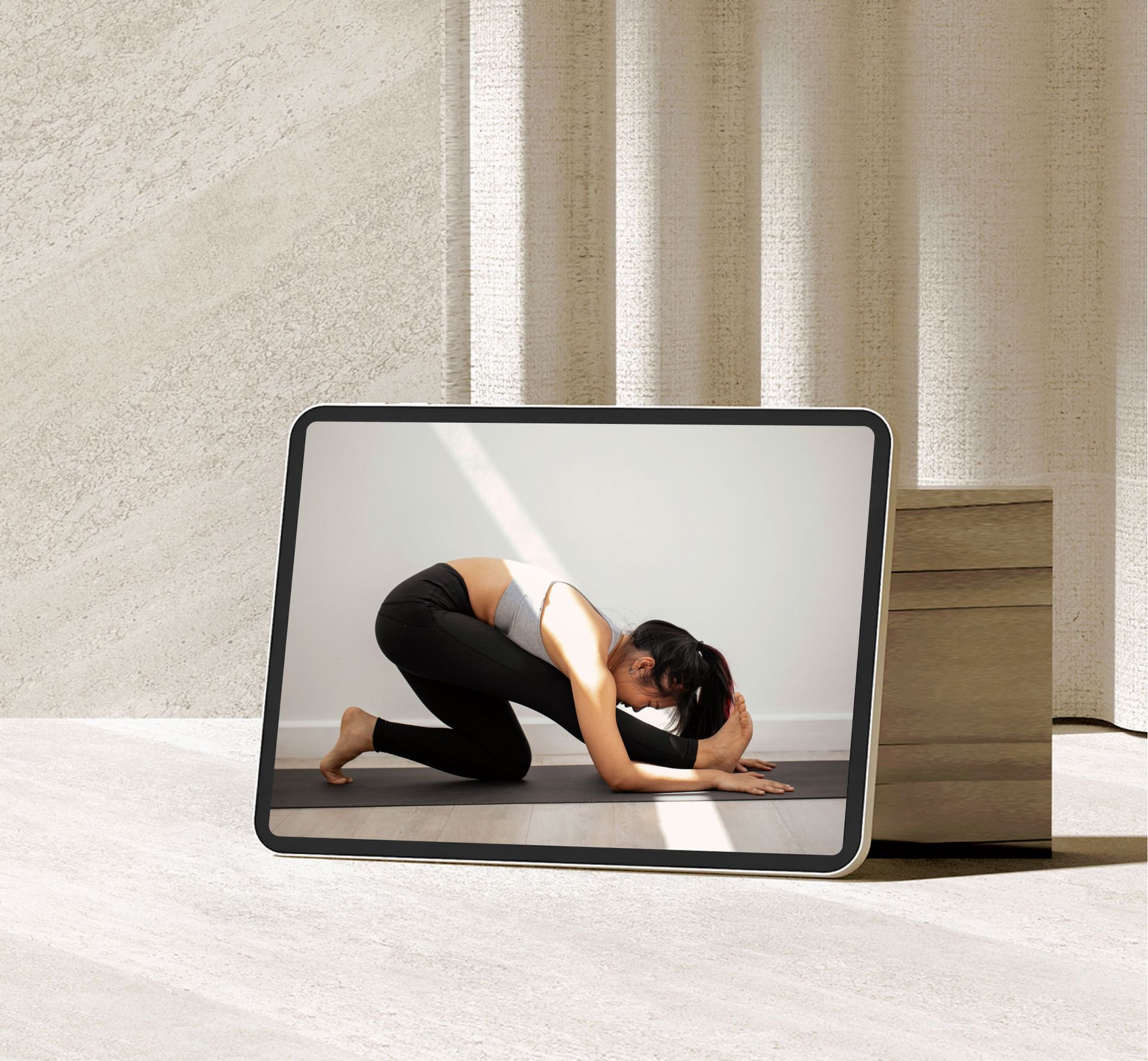 Tablet on the floor showing a woman doing a yoga pose in a bright room