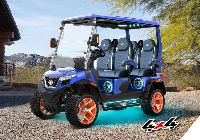 Blue and orange 4x4 golf cart with seating for six, parked on gravel with a desert backdrop and cabin.
