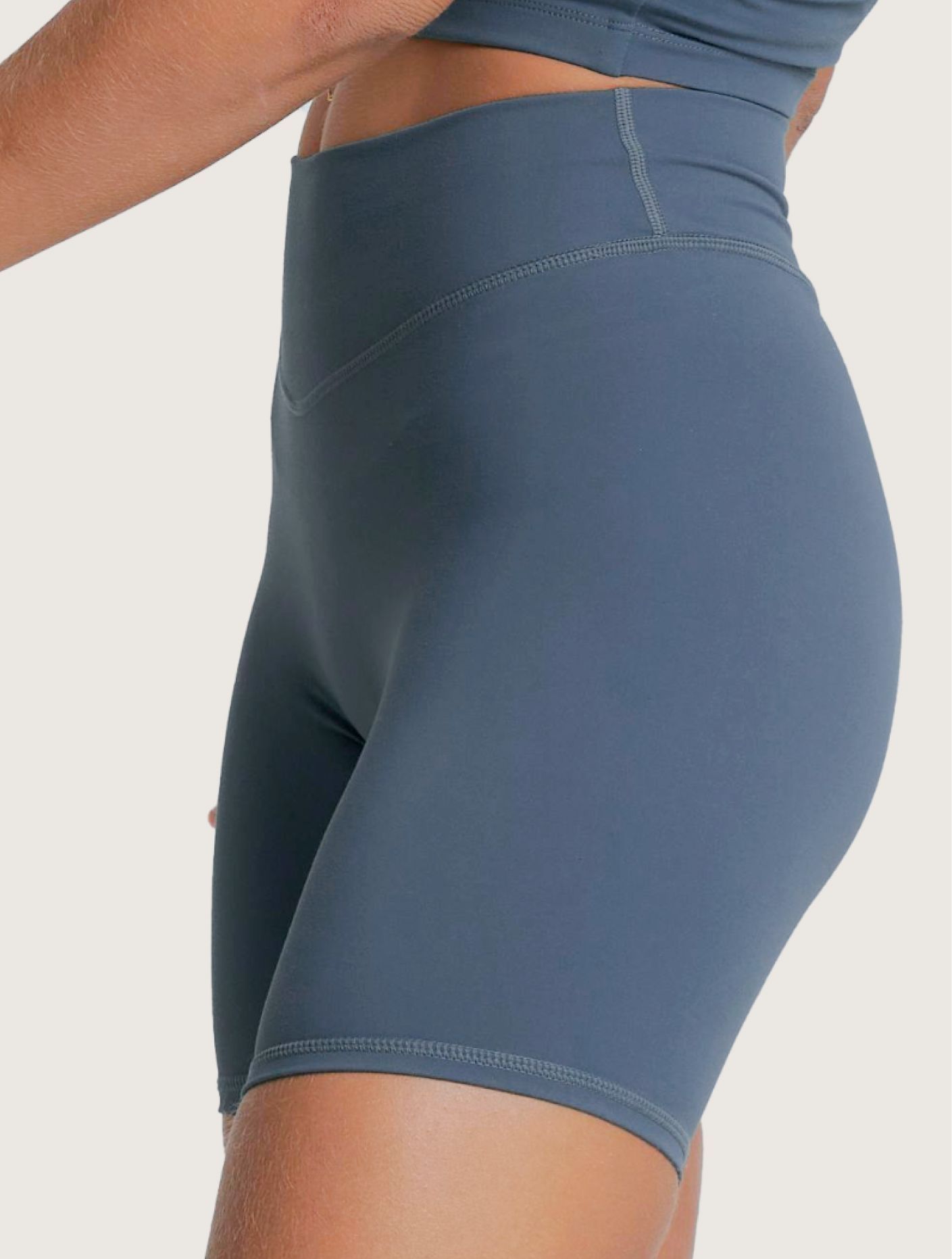 Model wearing blue cropped workout top and matching high-waisted bike shorts on a plain background