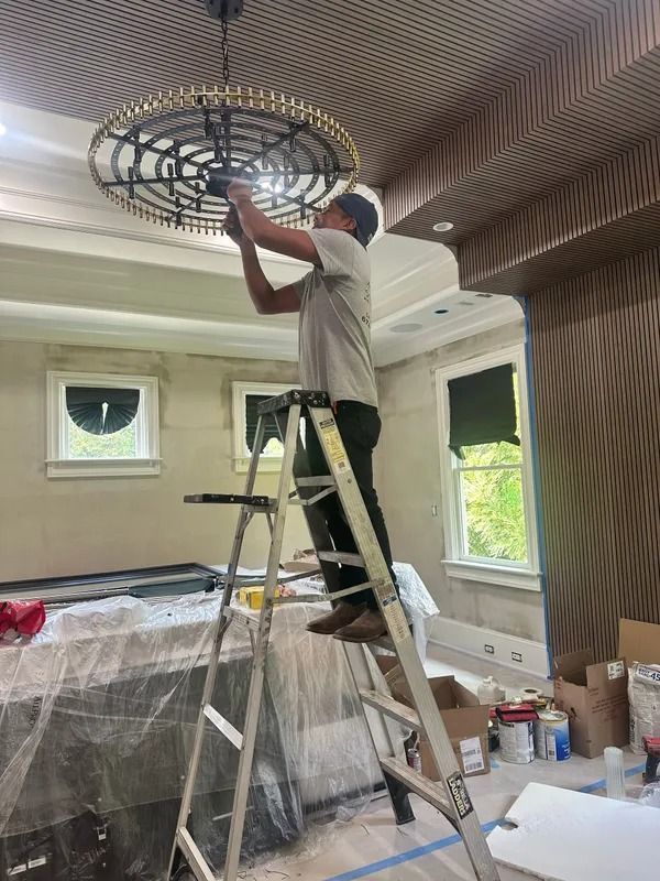 Person on a ladder installing a circular ceiling light fixture in a room under renovation.