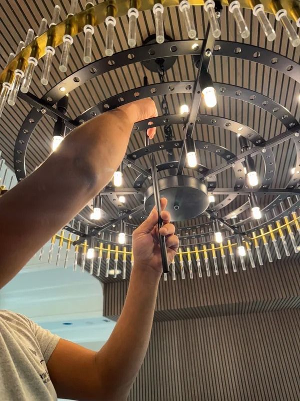 Person adjusting a circular ceiling light fixture with many hanging bulbs