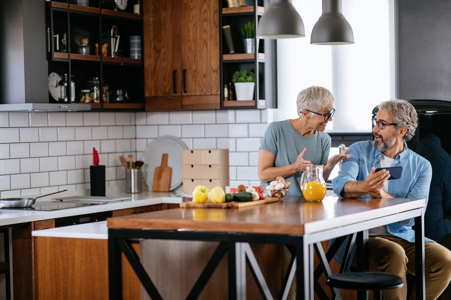Two people talking at a kitchen island with fruit and drinks in a modern black-and-white kitchen