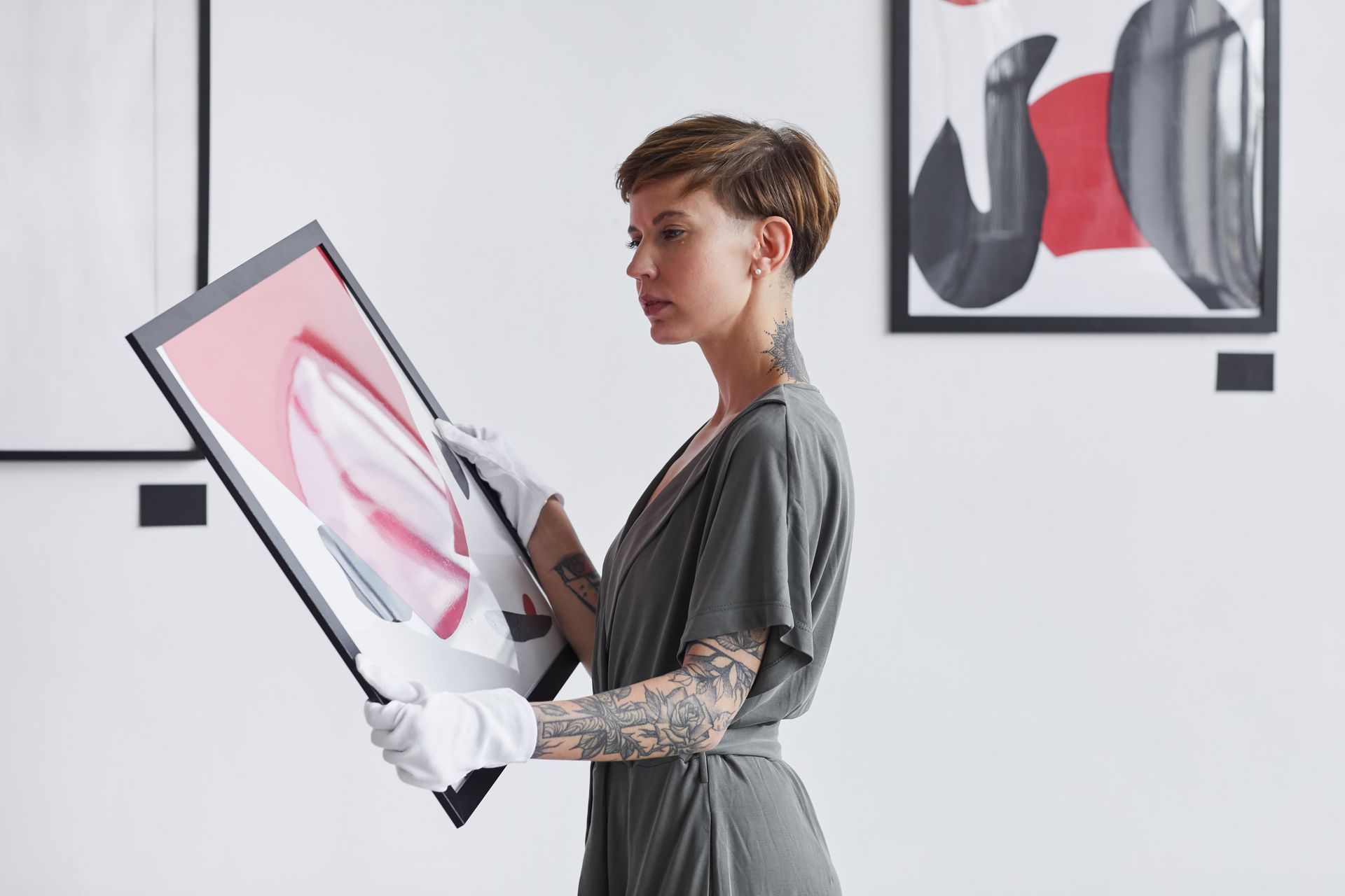 Woman holding a framed abstract print in a bright gallery, with another artwork on the wall.
