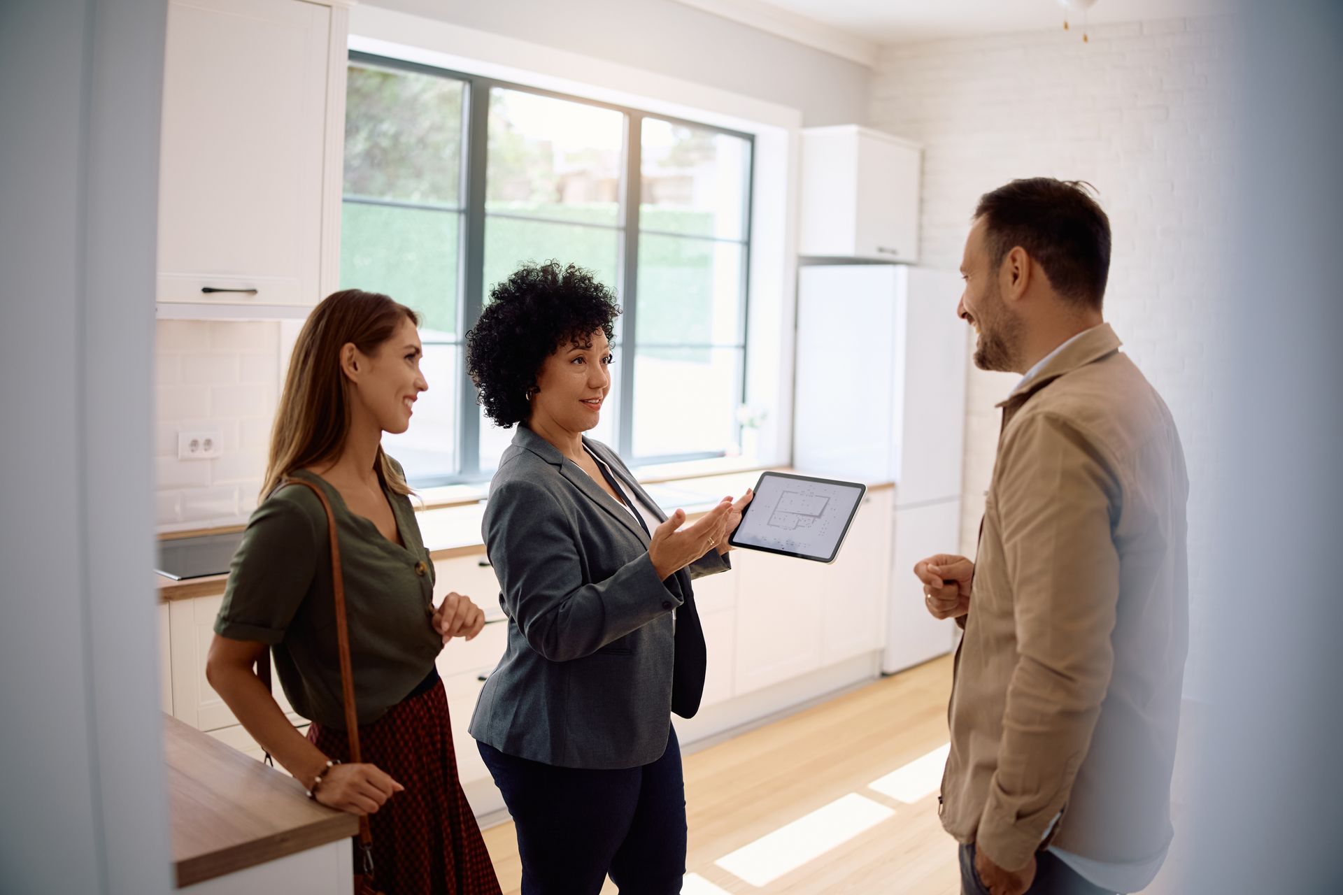 Two people talking with a clipboard in a bright kitchen with a third person nearby