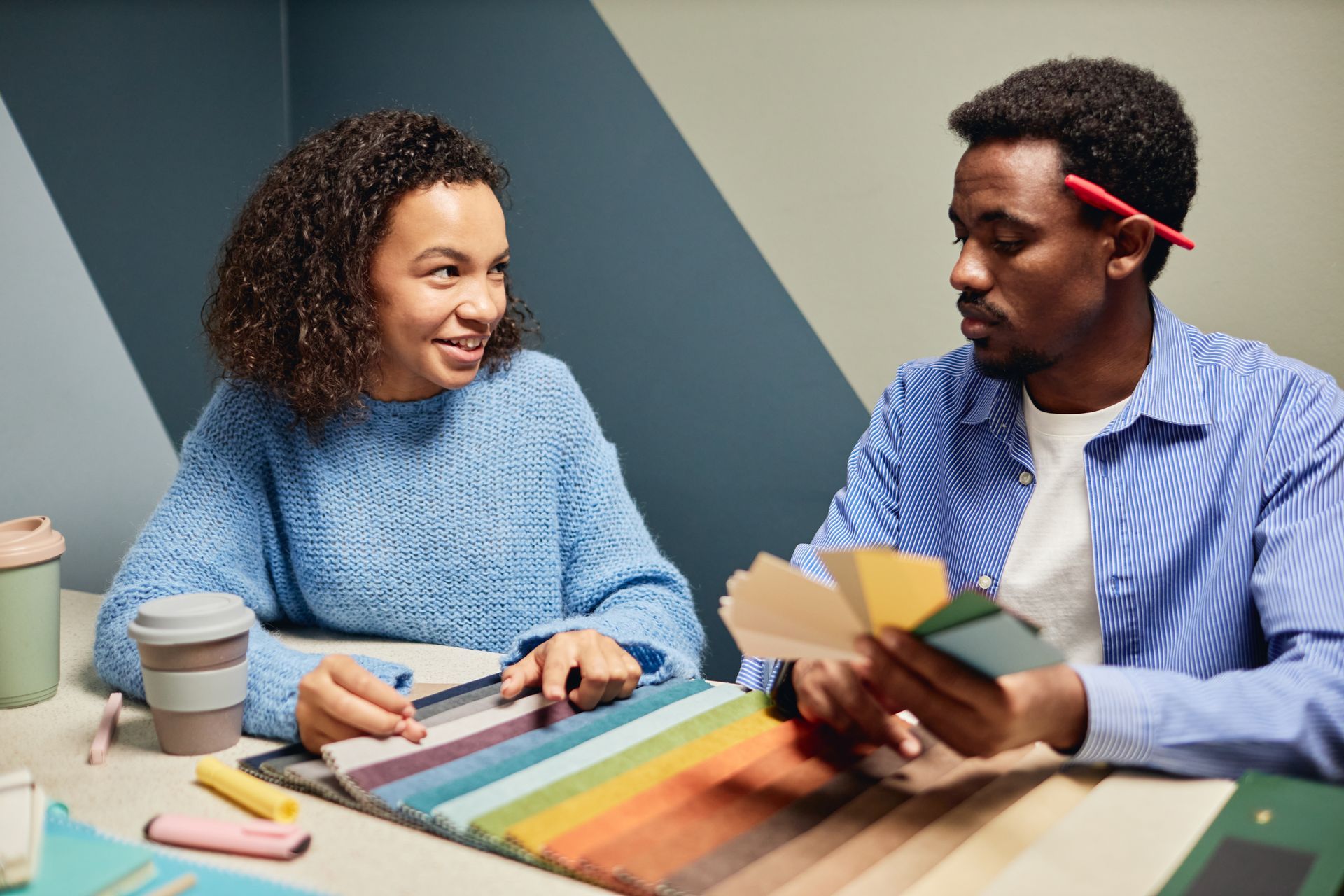 Two people at a table comparing colored paper samples in a creative workspace