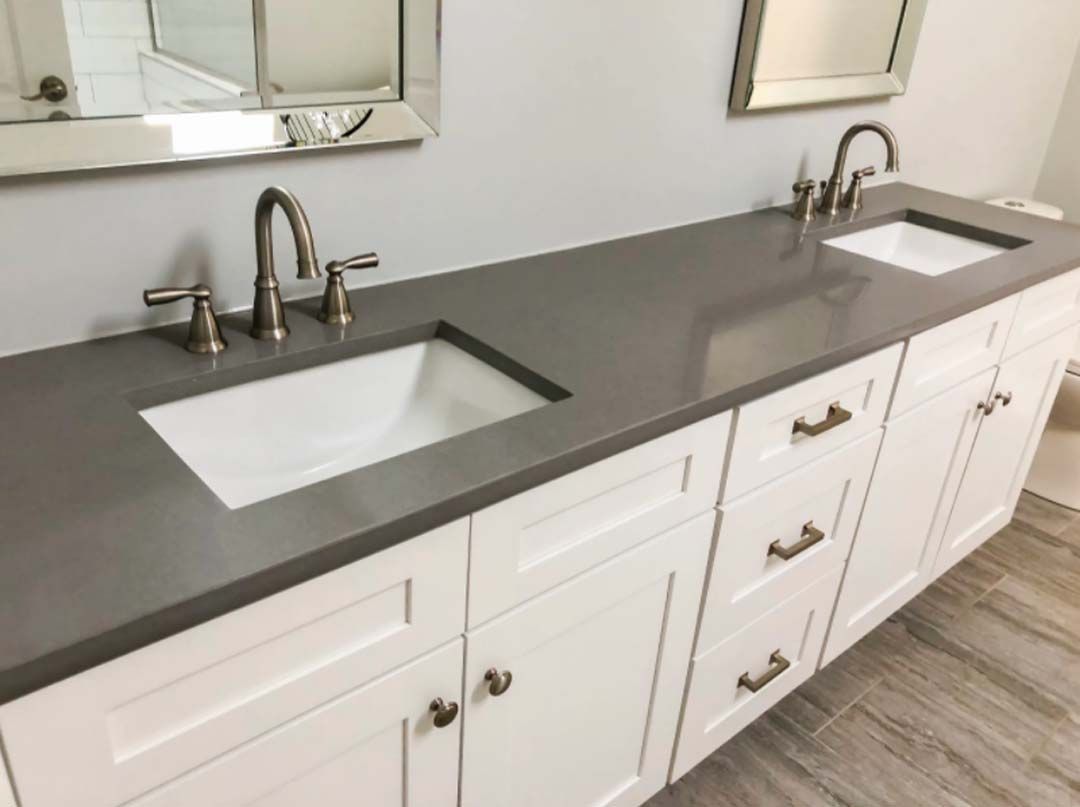 White bathroom vanity with two sinks, a grey countertop, and brushed nickel fixtures. Mirrors hang above the sinks.