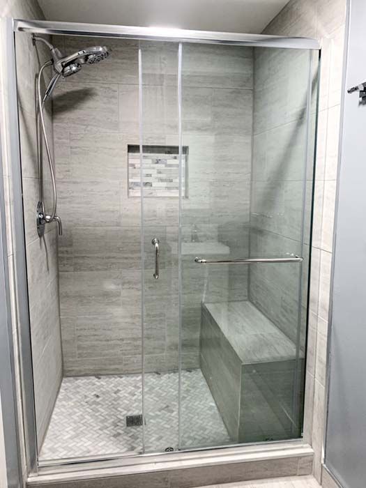 A modern, tiled shower stall with a glass door, built-in bench, and shower head. The shower features gray and white tones.