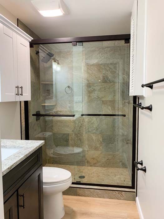 Bathroom with a dark-framed glass shower, toilet, vanity, and a white cabinet. Neutral-toned tile and wood flooring.
