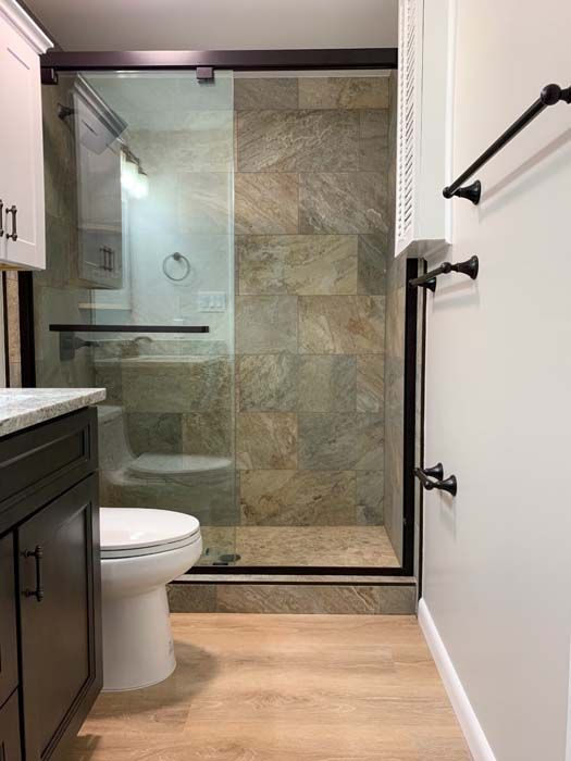 Small bathroom with a walk-in shower, toilet, and vanity. The shower has dark framing, a stone tile wall, and a glass door.